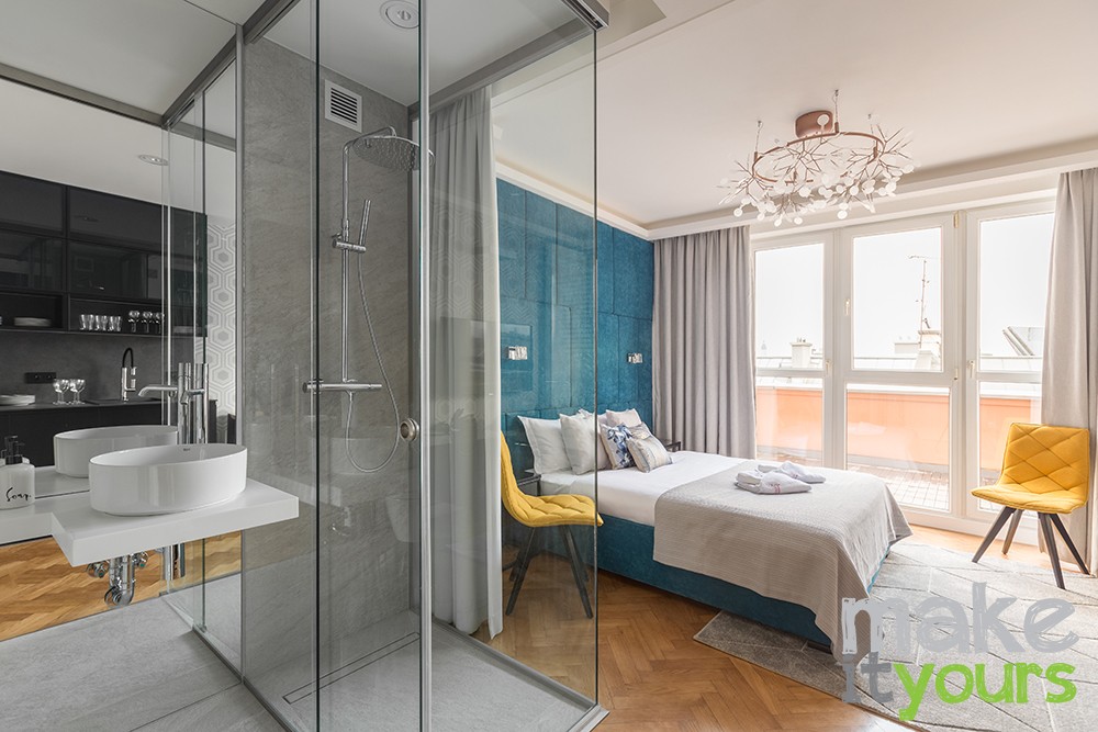 Zdjęcie przedstawia apartament w którym znajduje się przeszklona łazienka w sypialni. Projekt wnętrz od biura Make It Yours z Krakowa