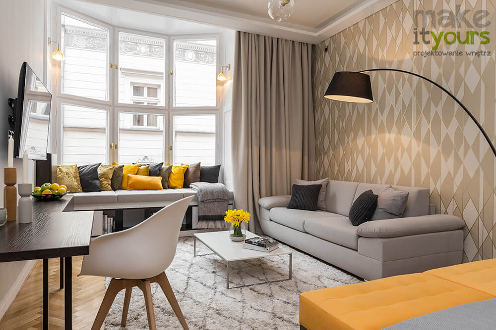 Zdjęcie wnętrz nowoczesnego salonu w apartamencie hotelowym, w kolorach szarości i pomarańczy zaprojektowane przez biuro projektowania wnętrz Make It Yours.