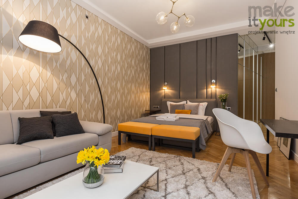Zdjęcie wnętrz nowoczesnej sypialni w apartamencie hotelowym, w kolorach szarości i pomarańczy, zaprojektowane przez biuro projektowania wnętrz Make It Yours.