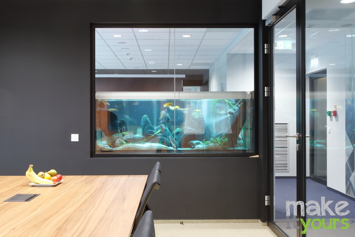 Zdjęcie wnętrz biura ANT, Sala konferencyjna, w ścianie duże akwarium z egzotycznymi rybami przez które widać recepcję. Projekt autorstwa Make It Yours - studio projektowania wnętrz.
