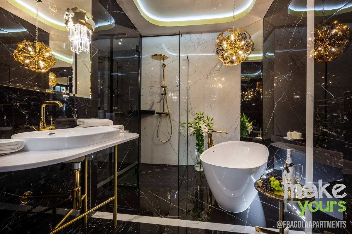 Zdjęcie przedstawia wnętrza łazienki wykonanej z ciemnego kamienia połączonego ze złotymi dodatkami i stylowym oświetleniem. Projekt wnętrz autorstwa Make It Yours - biura projektowania wnętrz z Krakowa