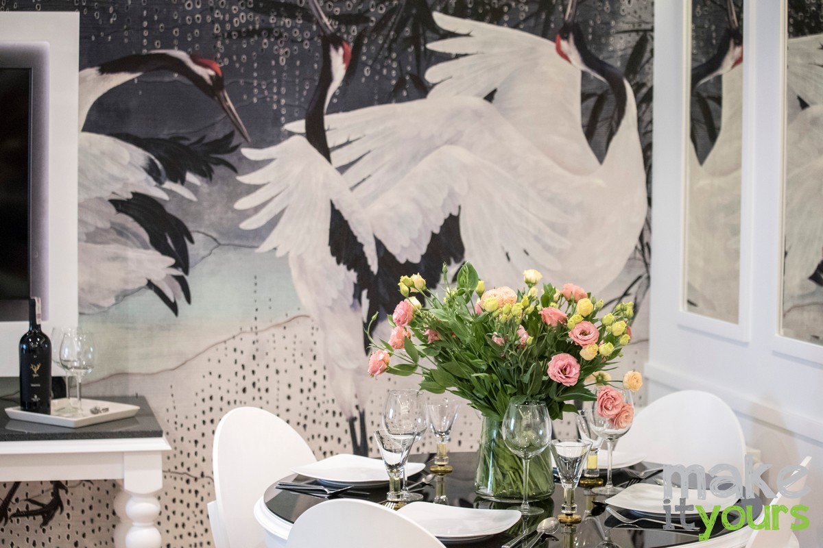 Zdjęcie fragmentu salonu, okrągły stół z bukietem kwiatów na tle tapety w żurawie, według projektu architekta wnętrz z biura Make It Yours z Krakowa