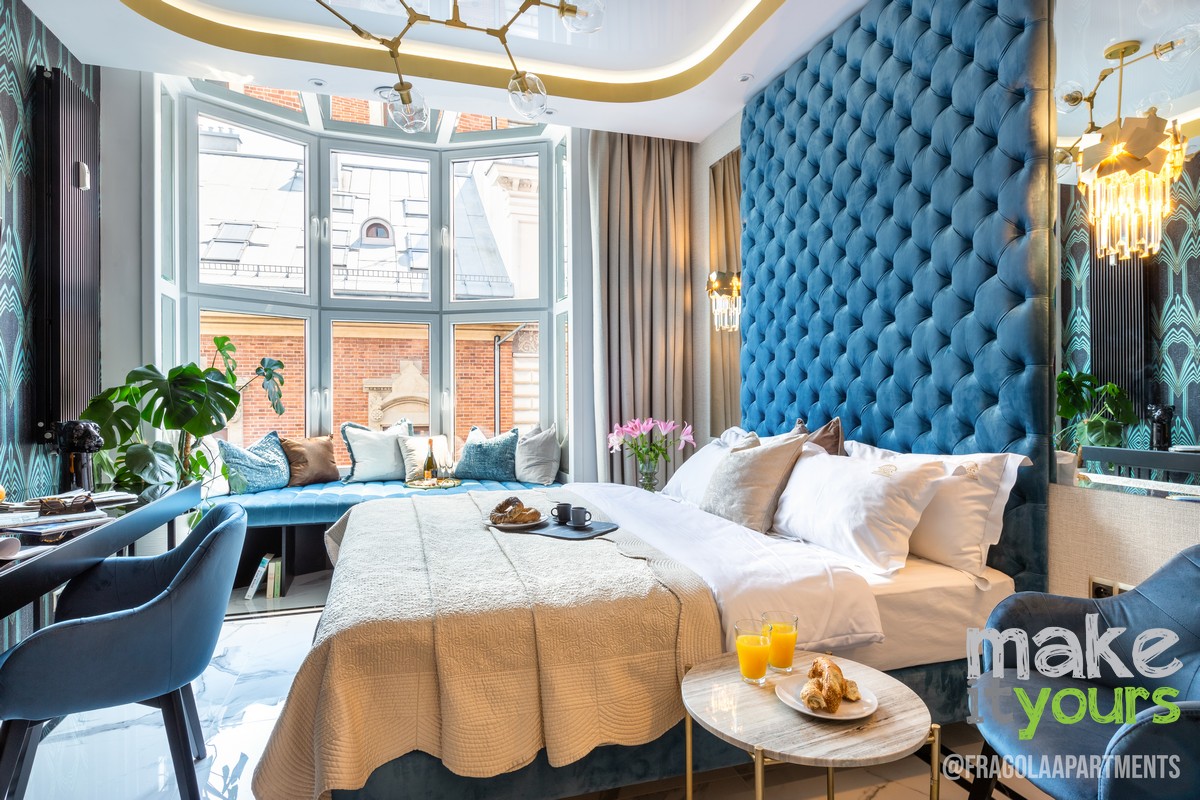 Zdjęcie przedstawia wnętrze dużej sypialni aparthotelu w starej kamienicy obok rynku w Krakowie. Widoczne są duże wezgłowie w kolorze niebieskim, złote dodatki, Aranżacja według projektu wnętrz biura projektowania wnętrz Make It Yours